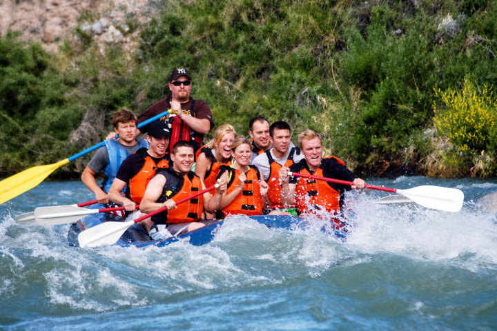 Group of people white-water rafting on a river, wearing life jackets.
