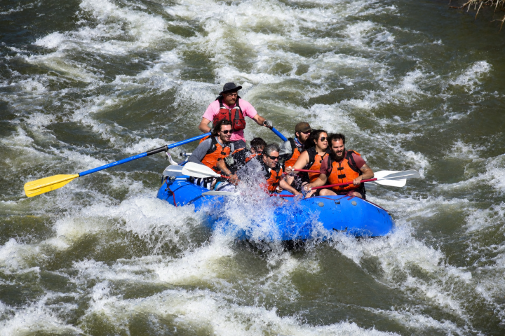 Group of people in blue raft navigating whitewater rapids.