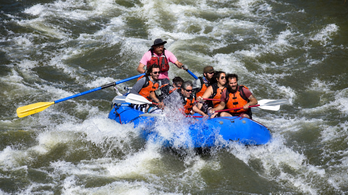 Group of people in blue raft navigating whitewater rapids.