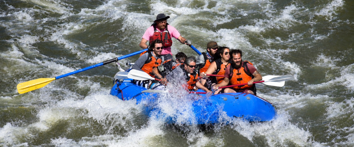 Group whitewater rafting in a blue raft on a turbulent river.