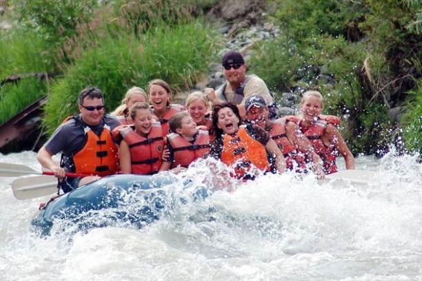 Group rafting down a river, wearing life jackets, with splashing water.