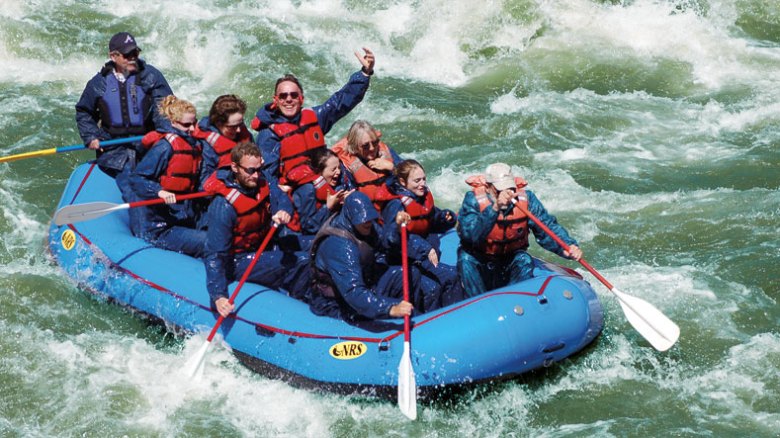 Group of people whitewater rafting on a river in a blue inflatable raft.